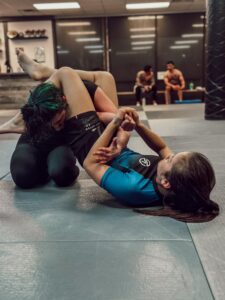 Two female BJJ practitioners are engaged in a grappling session on the mat, practicing submission techniques.
